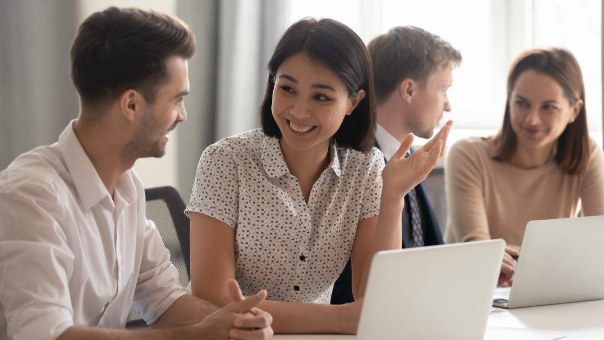 Young men and women speaking while working together on laptop computers.