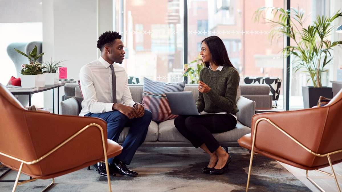 Businesswoman Interviewing Male Job Candidate In Seating Area Of Modern Office