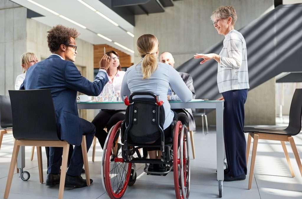 A woman in a wheelchair is seated at a table with colleagues during a work meeting.