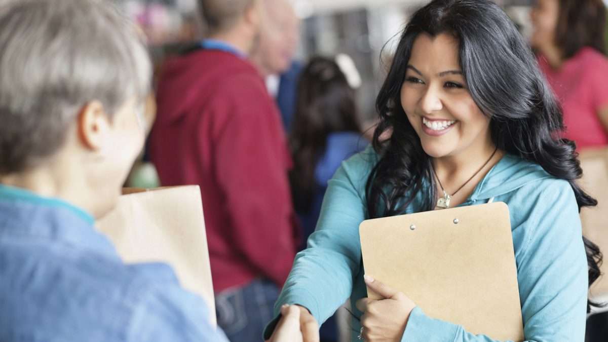 A woman holding a clipboard shakes hands with an employer at a job fair