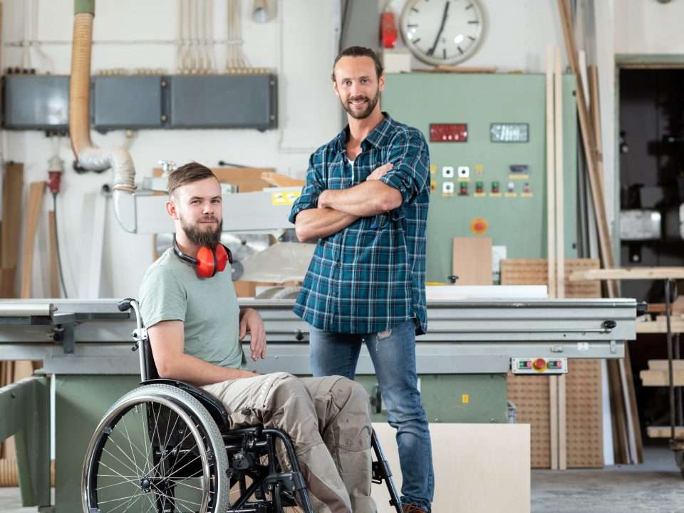 Un travailleur en fauteuil roulant et son collègue sont vus dans un atelier de menuiserie.