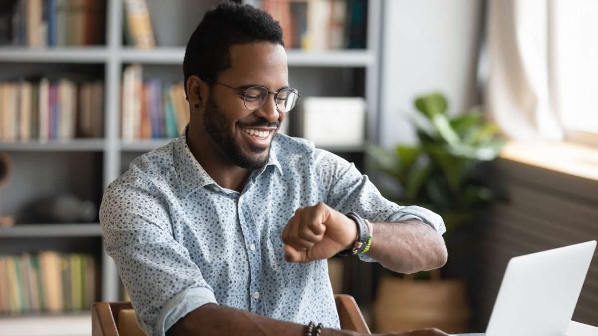 A man checks his watch while working at a laptop computer.