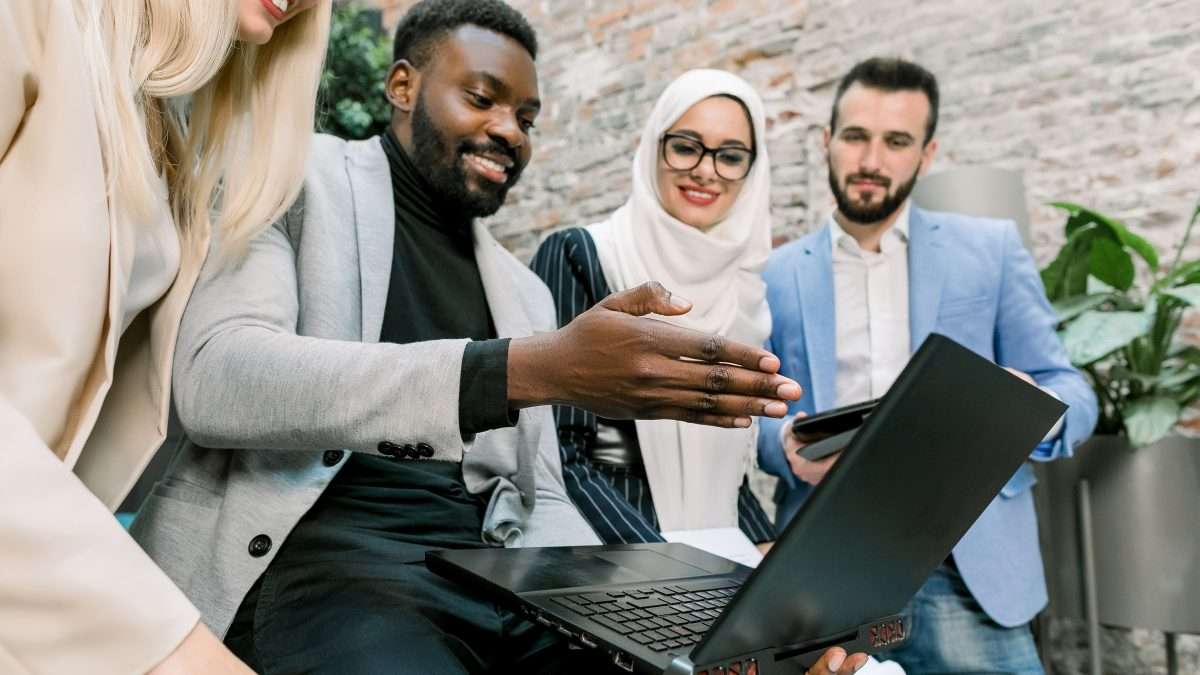 A team of employees from different cultures smile while looking at their colleague’s laptop computer screen.