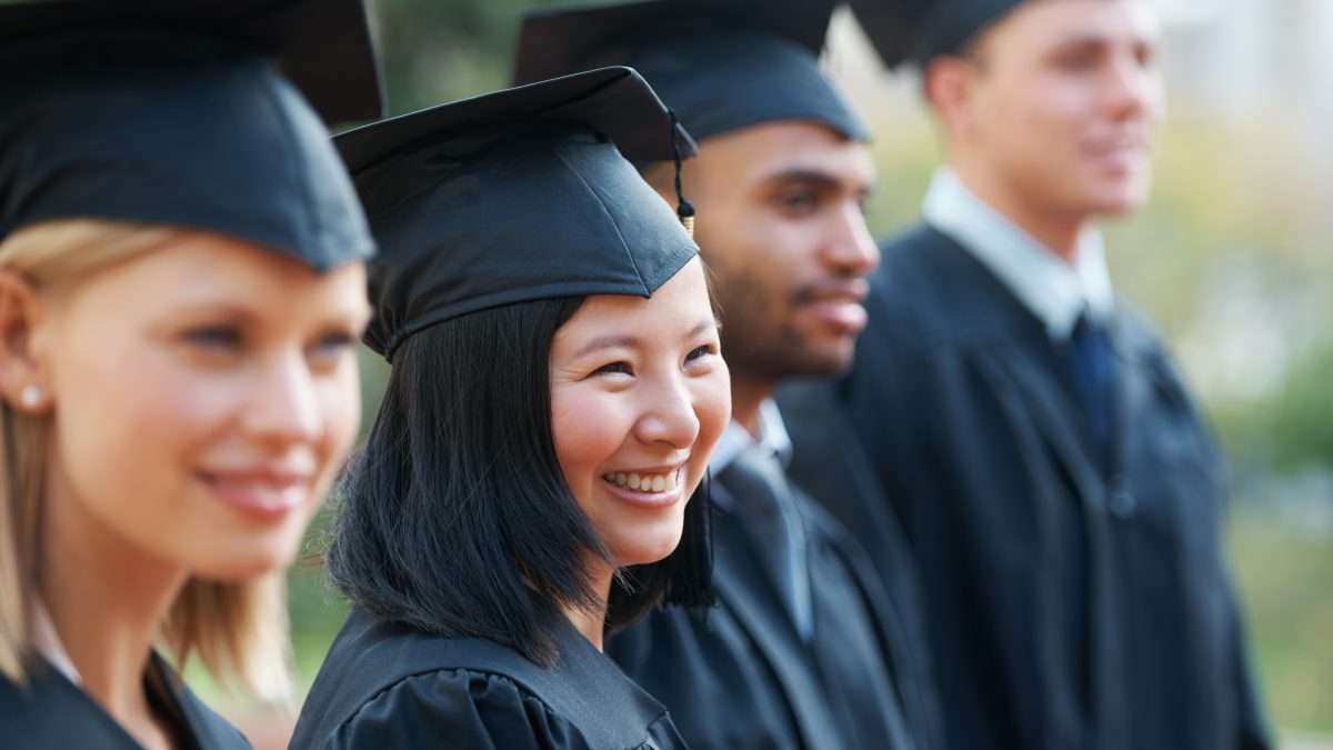 A group of post-secondary students smile as they pose in graduation caps and gowns.