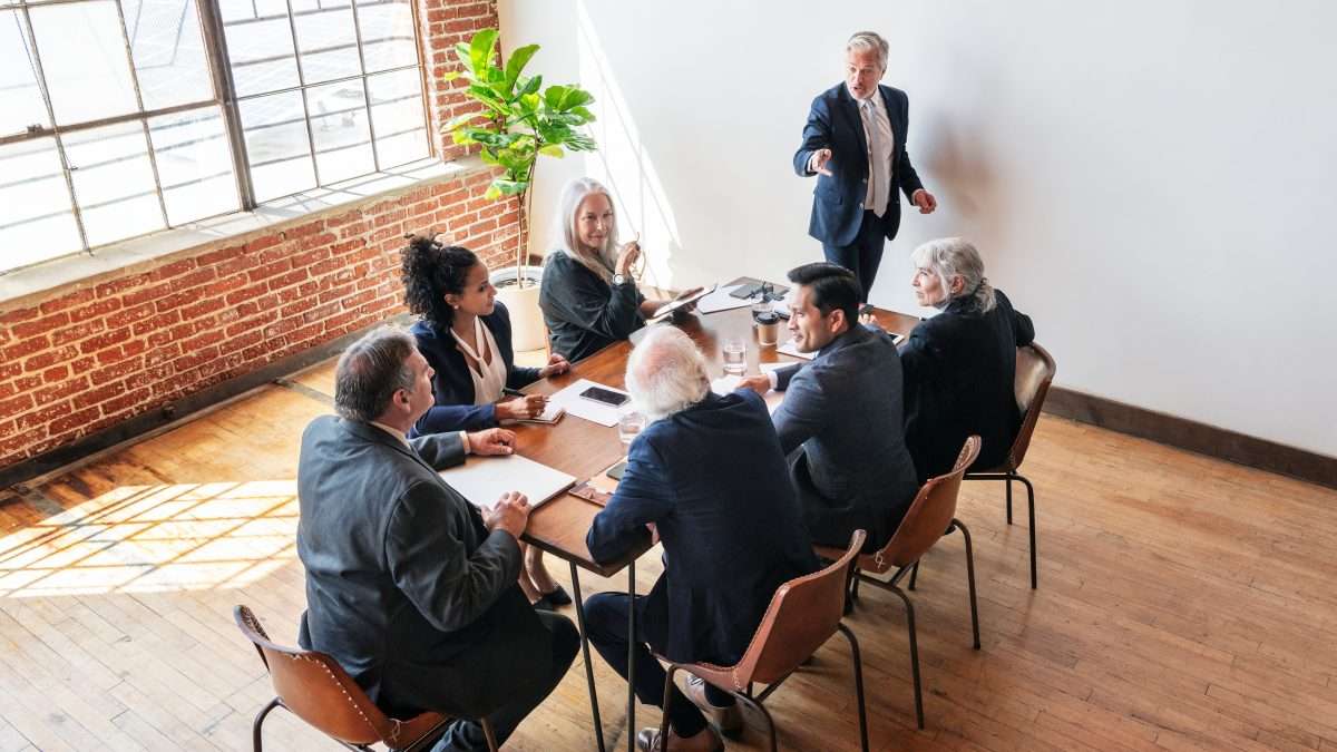 A diverse group of senior managers sit around a table as they attend a meeting in a boardroom.