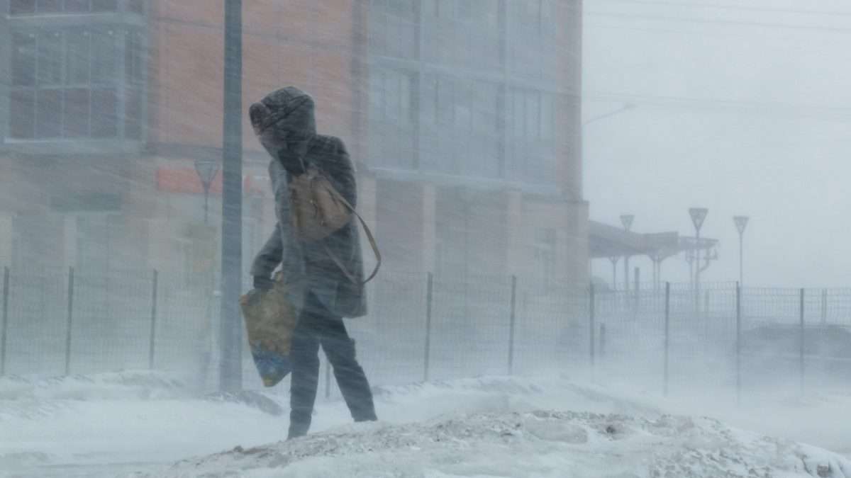 A woman walks through a city downtown in the midst of a winter snowstorm.